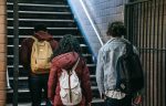 Three young people wearing backpacks walking up some stairs.